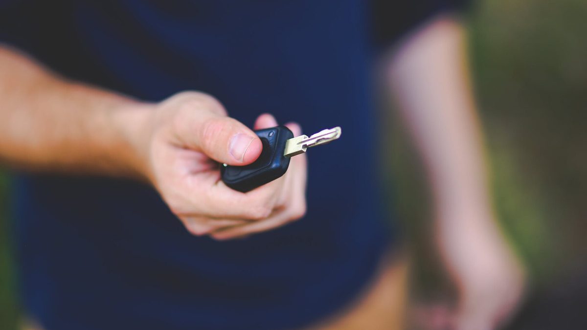 Main tendant une clé de voiture neuve, symbole de l’achat ou de la location d’un véhicule
